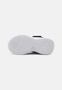 Chaussure de sport noire comprenant une semelle extérieure en caoutchouc blanc texturé avec des motifs rainurés pour une traction et une stabilité optimales.