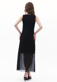Černé bezramínkové šaty s průhlednou krajkovou spodní částí, přiléhavým korzetem a dlouhou délkou. Hladká textura a jemné průhledné detaily na lemu.