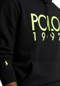 Sudadera con capucha negra con un gran estampado en verde neón "POLO 1992" en el frente y un pequeño logo en el puño. Tejido suave, ajuste relajado.