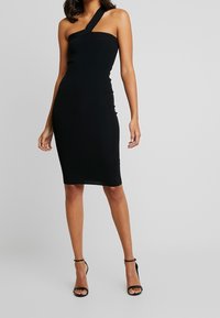 Robe midi noire moulante avec une bretelle unique. Fabriquée en tissu extensible à texture lisse, présentant un design épuré et minimaliste.