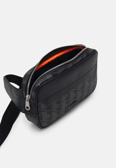 Sac bandoulière noir à motifs avec une finition lisse, doté d'une fermeture éclair, d'un intérieur orange et d'une bandoulière réglable.