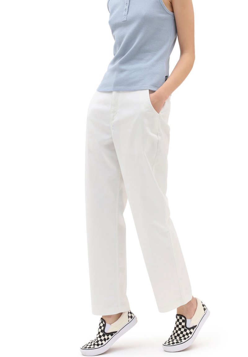 Pantalon large en coton blanc avec poches avant, associé à un débardeur bleu clair et des chaussures slip-on à damier noir et blanc.