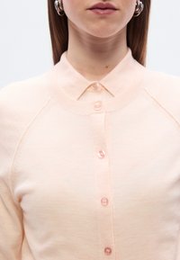 Ροζ ανοιχτό ροζ ζακέτα με γιακά σε σχήμα σημείου και κούμπωμα με κουμπιά. Διαθέτει μαλακή πλεκτή υφή και στρογγυλεμένες ραφές στους ώμους.