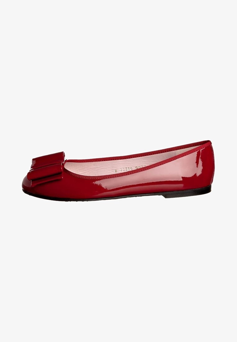 Ballerines en cuir verni rouge avec un nœud prononcé sur le bout, forme arrondie, texture lisse et semelle noire minimaliste.