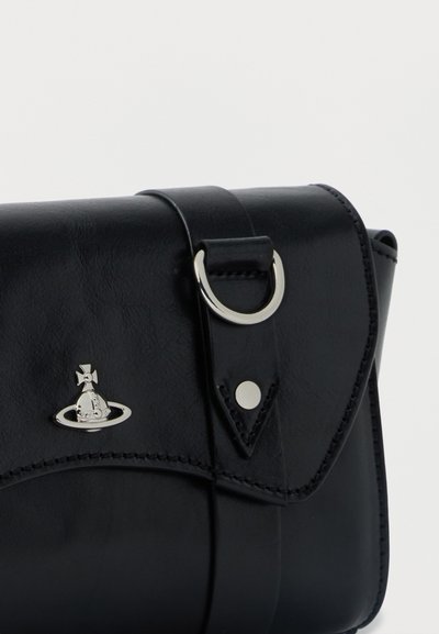 Μαύρη δερμάτινη τσάντα με ασημένιο κούμπωμα και διακοσμητικό μεταλλικό λογότυπο ενός πλανήτη με σταυρό πάνω του στην πτυχή, πάνω σε μονόχρωμο φόντο.