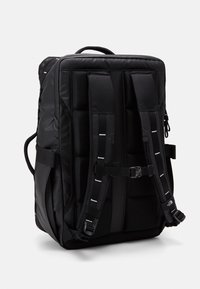 Svart ryggsäck med vadderad design, justerbara axelremmar och flera externa fickor. Tillverkad av slitstarkt tyg med texturerad yta.