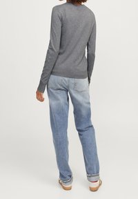 Grå tröja med rund halsringning, långa ärmar och ribbad mudd, i kombination med ljusblå, löst sittande jeans och vita skor.