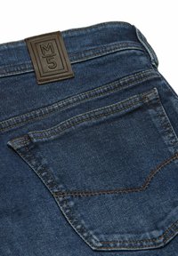 Donkerblauwe denim spijkerbroek met een gestructureerd oppervlak, voorzien van contrasterende bruine stiksels en een leren label met "M5" op de tailleband.