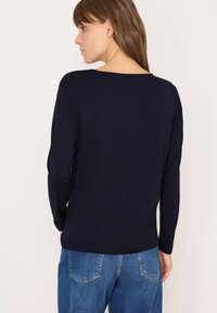 Marineblauwe lange mouwen top van zacht materiaal, met een ronde hals en een aansluitend ontwerp. Gepaarde met lichtblauwe spijkerbroek.