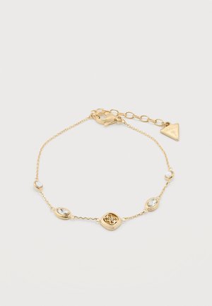 Delicate gold chain bracelet with clear oval gemstones, a central gold emblem, and a triangular brand tag near the clasp for adjustable length.