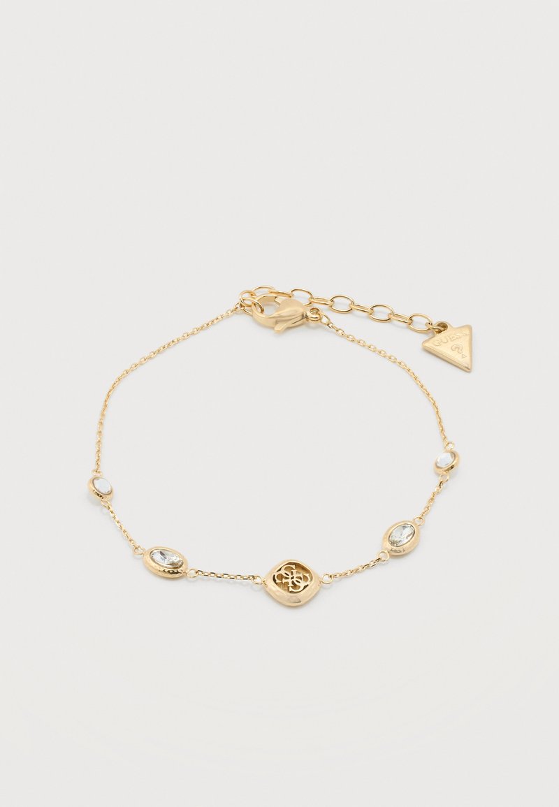 Λεπτό χρυσό βραχιόλι με διάφανα οβάλ πολύτιμους λίθους, κεντρικό χρυσό έμβλημα και τριγωνική ετικέτα της μάρκας κοντά στο κούμπωμα για ρυθμιζόμενο μήκος.