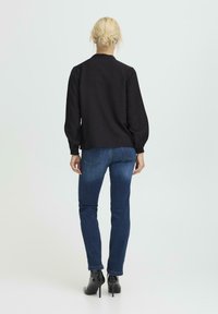Schwarze Bluse mit langen Ärmeln und lässiger Passform, mit gerafften Manschetten, kombiniert mit dunkelblauen Jeans und schwarzen Stiefeletten mit Absatz.