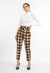Witte coltrui gecombineerd met bruin gestreepte broek met een crème ruitpatroon en strikdetail aan de taille. Model draagt zwarte hoge hakken.