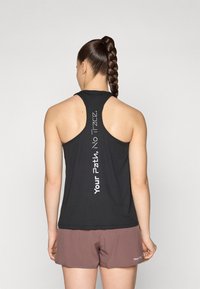 Svart sportstopp med ribbet tekstur, racerback-design, og hvit tekst "Din vei, ingen spor" som går vertikalt langs ryggen.