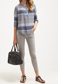 Blusa a maniche tre quarti con motivo navy e bianco, abbinata a pantaloni grigi attillati e una borsa nera. Sandali neri piatti completano il look.