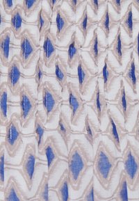 Witte stof met blauwe en beige diamantpatronen, voorzien van plooien die een verticale textuur en lichte schaduwen creëren.