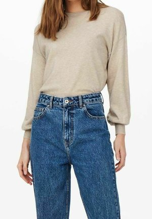 Haut beige à manches longues associé à un jean bleu taille haute. Le haut a une texture douce, tandis que le jean présente une décoloration et une coupe classique.