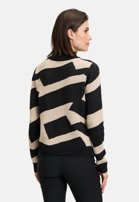 Knit sweater featuring a black and beige zigzag pattern. Ribbed collar and cuffs, with a relaxed fit and soft texture.