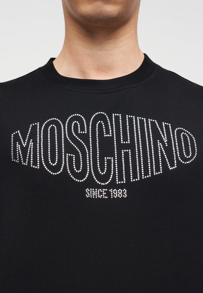 Μαύρο βαμβακερό t-shirt με τη λέξη "MOSCHINO" σε λευκά στρας, με το έτος "1983" από κάτω, στρογγυλή λαιμόκοψη και κοντά μανίκια.