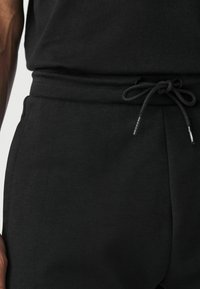 Pantalones de chándal negros de algodón con cintura ajustable, que presentan una textura suave y bolsillos laterales para mayor funcionalidad.