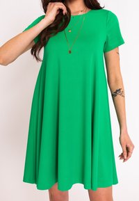 Grünes Kurzarmkleid mit lockerer Passform, aus glattem Stoff gefertigt. Es hat einen runden Ausschnitt und einen ausstellenden Saum, der bis zur Mitte des Oberschenkels reicht.