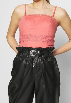 Vrouw draagt een mouwloze roze cropped top met kanten details en zwarte leren broek met hoge taille, een gerimpelde taille en een zilveren gesp riem.
