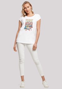 Hvit T-skjorte med et fargerikt grafikk av kvinnelige superhelter og teksten "Femme Power." Kombinert med hvite slim-fit bukser og hvite sneakers.