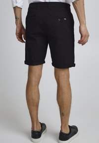 Schwarze lässige Shorts mit umgeschlagenen Säumen, aus Baumwolle, ausgestattet mit zwei Gesäßtaschen mit Knöpfen und minimalistischem Design.