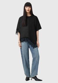 Sort oversized top med blondekant, parret med lyseblå vide ben jeans og sorte spidse sko. Glat stof med delikate blonde detaljer.