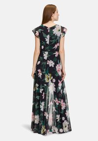Robe maxi florale en tissu noir transparent, avec des fleurs roses et blanches, manches volantées et silhouette fluide. Vue de dos présentée.