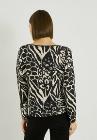 Pull à manches longues en tissu doux avec un motif animalier noir et beige, doté d'un large col et d'un ourlet côtelé.