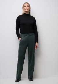 Svart figurnära polotröja som är kombinerad med löst sittande, mörkgröna byxor med bälte i midjan och sidofickor. Slät tygtextur.