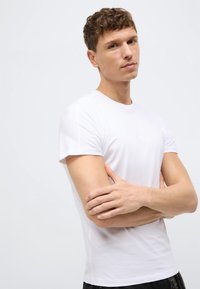 Λευκό βαμβακερό t-shirt με στρογγυλή λαιμόκοψη και κοντά μανίκια, εφαρμοστή γραμμή, ομοιόμορφη υφή και χωρίς ορατά σχέδια ή γραφικά.