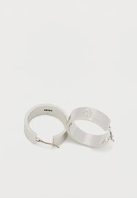 Srebrni uhani v obliki obroča z gladkim, polished zaključkom. Eden od uhanov ima vtisnjen logotip DKNY. Lahki z varnim zaponkom za pritrditev.