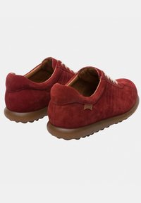 Scarpe in suede rosso con punta arrotondata, cuciture laterali texture, suola in gomma marrone e lacci piatti; con un logo discreto sul retro.