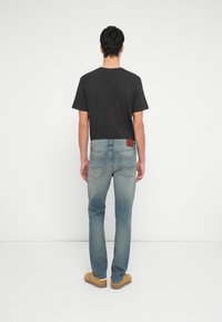 Camiseta negra de manga corta, jeans azul claro con un acabado texturizado, parche de cuero en la cintura, combinados con zapatos deslizantes color beige.