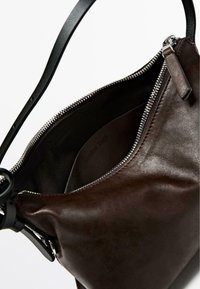 Borsa a mano in pelle marrone con una superficie liscia, dotata di una cerniera argentata e di una tracolla nera. L'interno presenta una fodera in tessuto scuro.