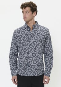 Cămașă cu mânecă lungă din material bleumarin și alb cu un model floral. Dispune de guler și închidere cu nasturi, textură netedă.