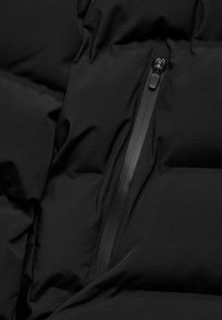Tessuto di giacca a vento nera con texture trapuntata; presenta una tasca con zip con un'impugnatura nera liscia; finitura morbida e opaca.