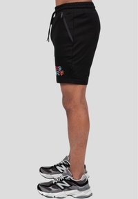 Sorte bomulds shorts med elastisk talje, sidelommer med lynlås og farverig "Stay Cool" broderi på venstre lår. Boret med sneakers.