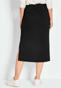 Schwarzer mittel-langer Rock aus dehnbarem Stoff, mit einem seitlichen Schlitz und einem elastischen Bund, kombiniert mit weißen Sneakers.