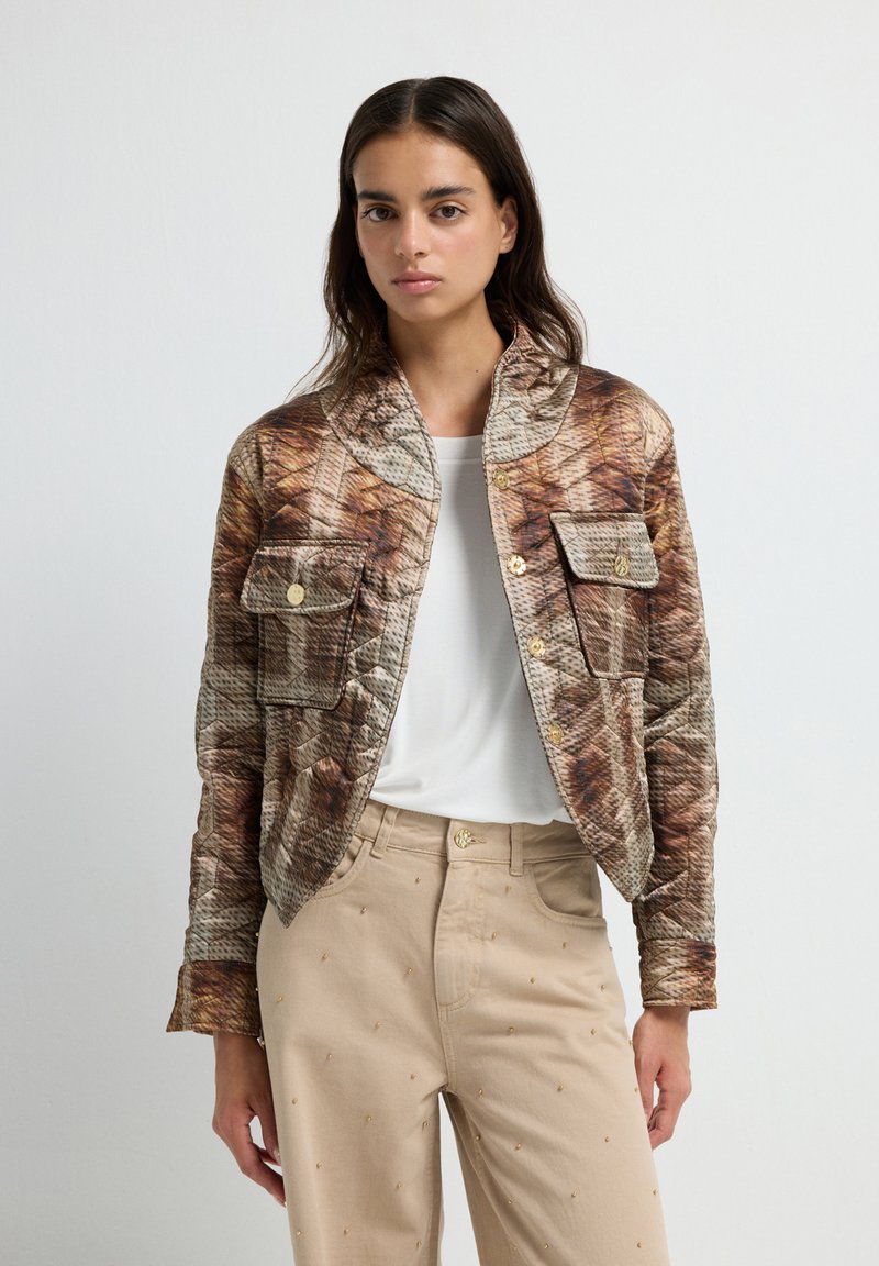 Chaqueta acolchada en tonos terrosos con un diseño estampado, que cuenta con un cuello, dos bolsillos frontales y botones en tono dorado. Combinada con pantalones beiges.