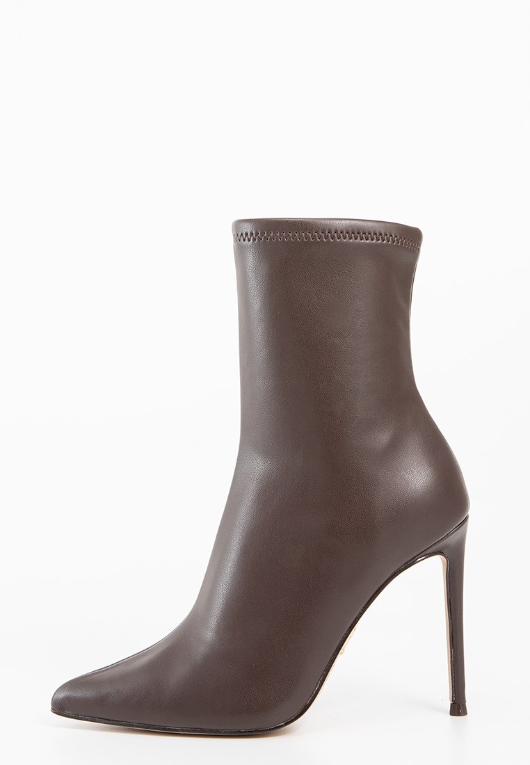 Bottine en cuir marron avec un bout pointu, un talon aiguille haut et une texture lisse. Elle présente un manchon cousu en haut.