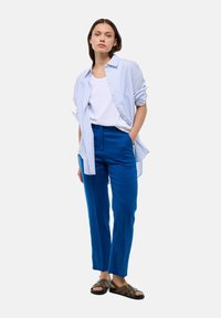 Chemise rayée bleu clair sur un débardeur blanc, assortie à un pantalon bleu vif et des sandales marron. Design simple avec une coupe décontractée.