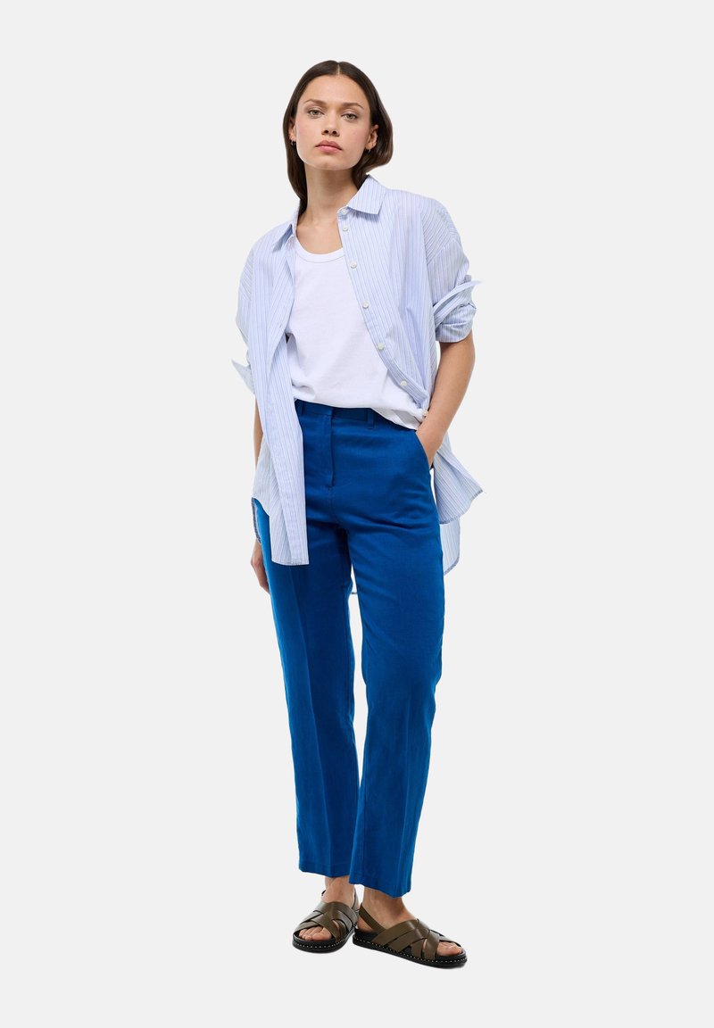 Chemise rayée bleu clair sur un débardeur blanc, assortie à un pantalon bleu vif et des sandales marron. Design simple avec une coupe décontractée.