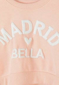 Tissu rose avec des lettres blanches en relief formant le mot « MADRID » au-dessus d'un symbole de cœur et « BELLA » en dessous.