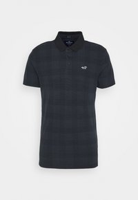 Camisa polo de cuadros negros hecha de tejido texturizado, con cuello, tapeta de dos botones y un pequeño logotipo blanco en el pecho.