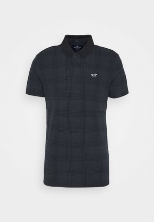 Camisa polo de cuadros negros hecha de tejido texturizado, con cuello, tapeta de dos botones y un pequeño logotipo blanco en el pecho.