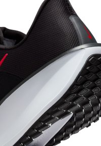 Zapatilla deportiva negra con parte superior de malla transpirable, detalle del logo rojo y suela de goma negra texturizada para mayor tracción. Mediasuela blanca y suave.