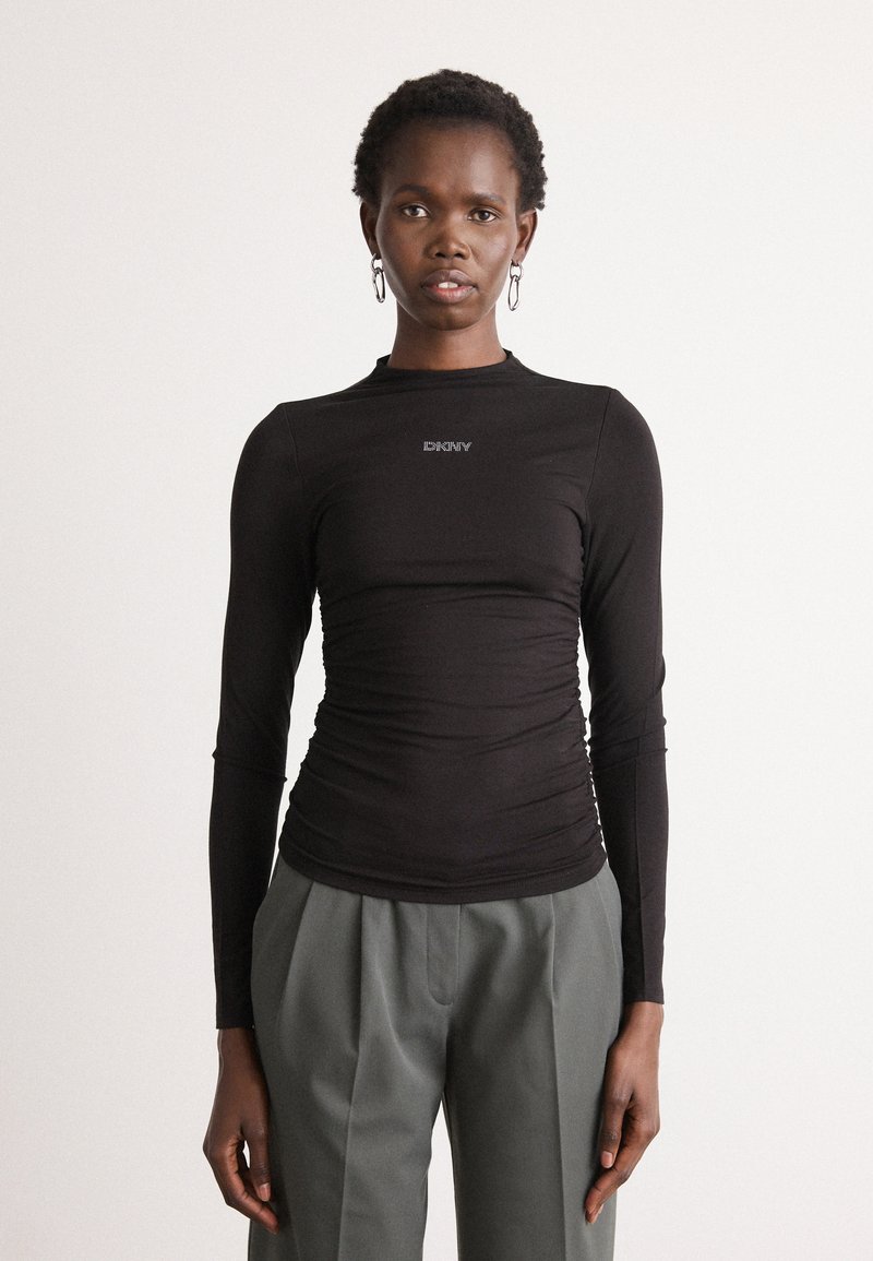 Black long-sleeve top featuring a ruched design and a subtle logo at the chest, paired with loose gray trousers for a contrast in style.